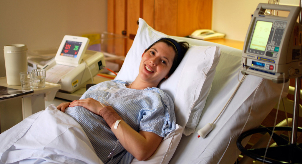 Heavily pregnant woman lying in a hospital bed being put on a drip and attached to a monitor