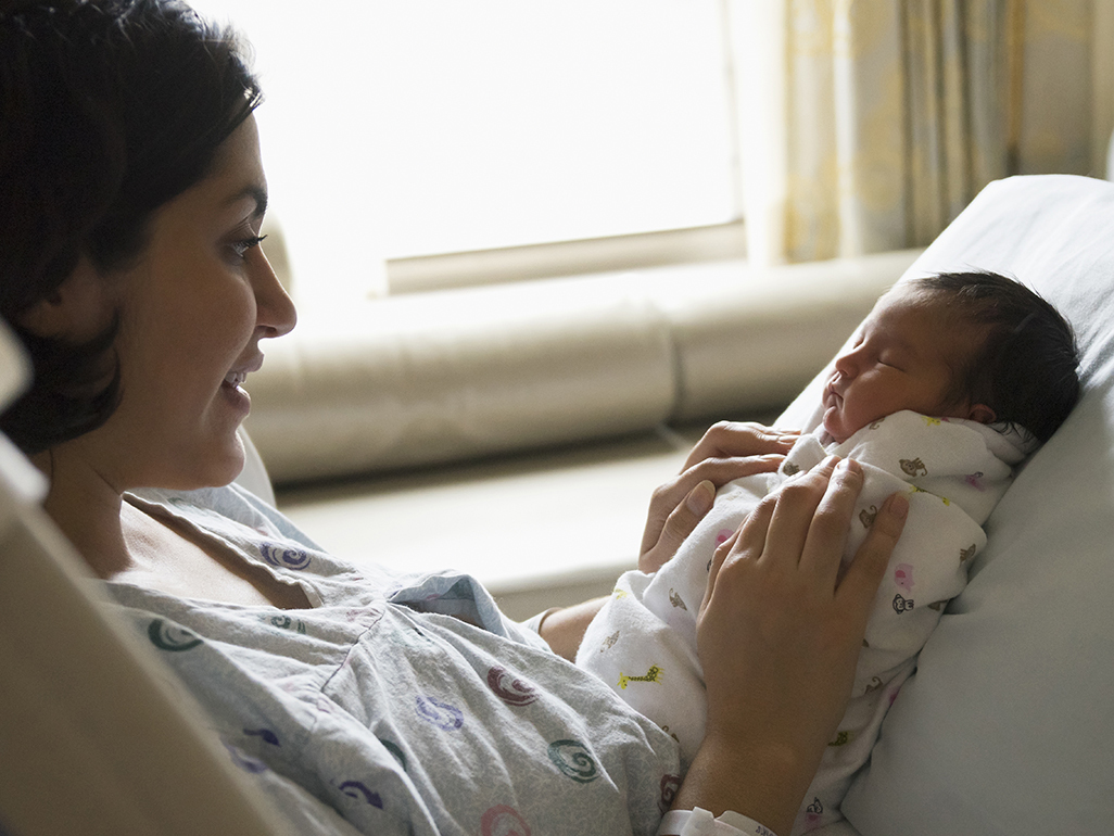 Woman lying on a hospital bed holding newborn baby