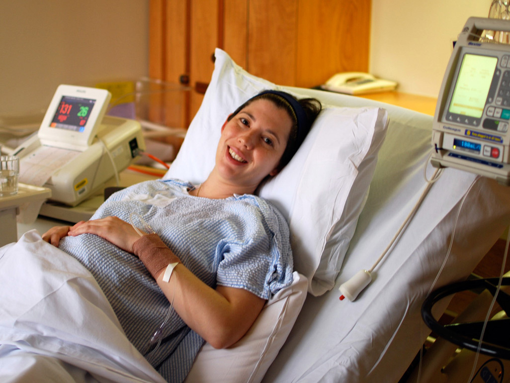 Heavily pregnant woman lying in a hospital bed being put on a drip and attached to a monitor